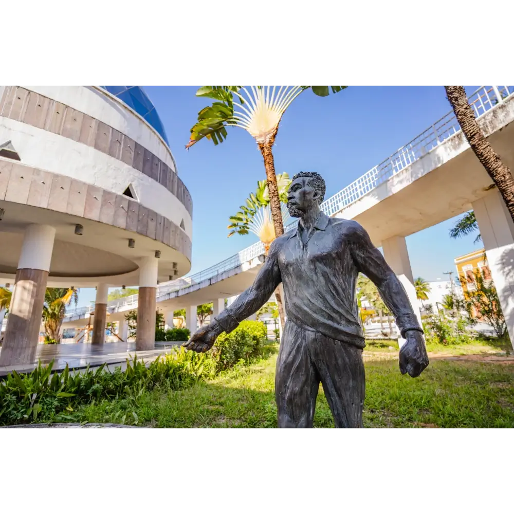 Estátua em bronze de Patativa do Assaré no Centro Dragão do Mar de Arte e Cultura, com a arquitetura moderna do centro cultural e passarelas ao fundo